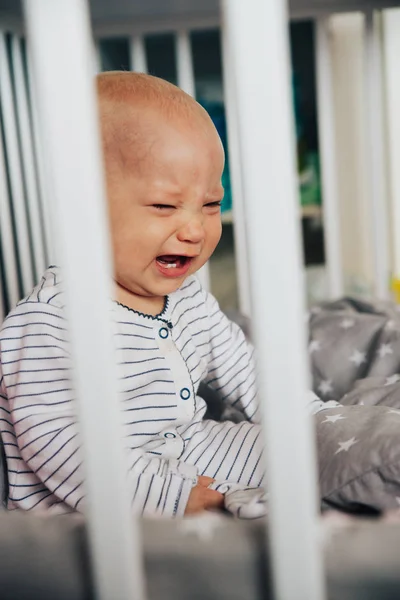 Baby girl with blue eyes and blond hair is crying in her bed — Stock Photo, Image