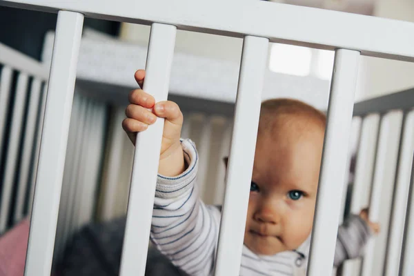 Baby girl with blue eyes and blond standing in her bed, close up on hand — Stock fotografie