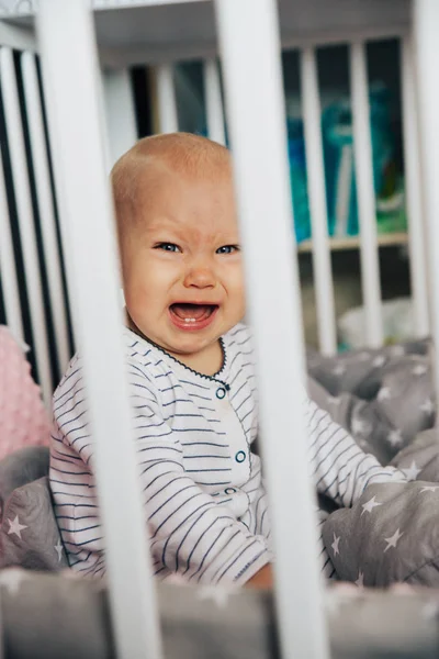 Baby girl with blue eyes and blond hair is crying in her bed — Stock Photo, Image