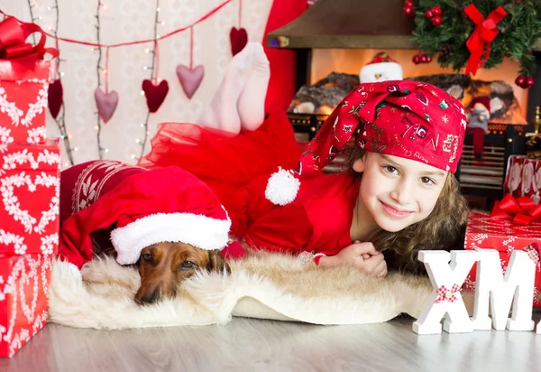 Niña en una gorra de Navidad se sienta con un perro en el Husky Chri —  Fotos de Stock