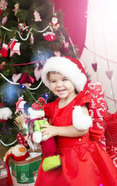 Liten söt flicka i röd tomte hatt dekorera nytt år träd — Stockfoto