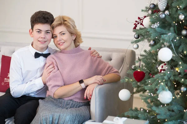 Mom and son decorate the Christmas tree. Mom and son cuddle near