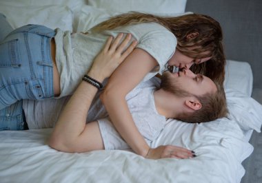 Genç bir çift evdeki düzgün bir yatakta nazikçe öpüşür ve sarılır.