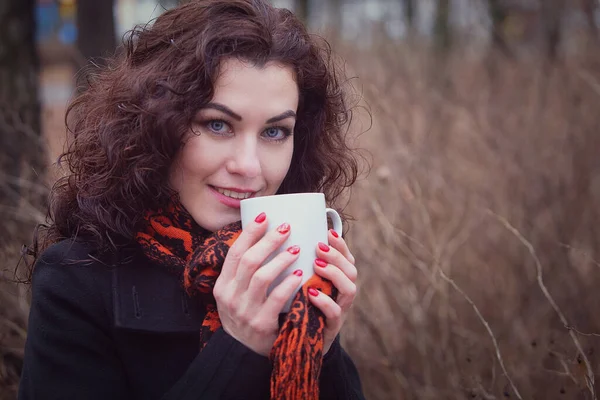 A frozen woman drinks her hot drink tea or coffee from a Cup.