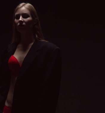 Karanlık bir odada, loş bir lambanın altında kırmızı iç çamaşırlı seksi bir kızın dramatik portresi.