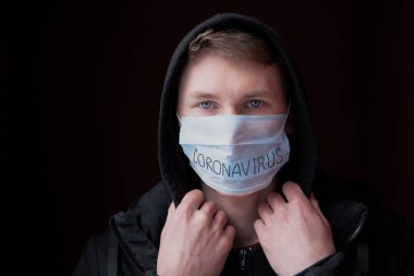 Kafasında kapüşonlu siyah bir ceket ve yüzünde Coronavirus yazan bir maske olan üzgün bakışlı genç yakışıklı bir adam.. 