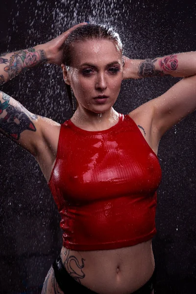 一个穿着红色内裤 有着美丽胸部的性感金发姑娘站在明亮的水柱下 调整着她湿透的头发 — 图库照片