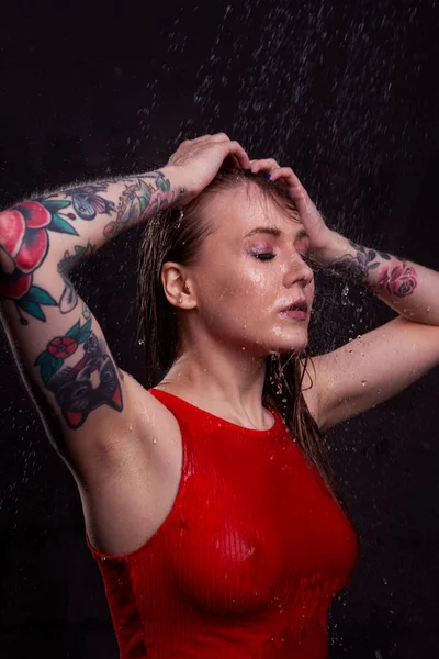 一个穿着湿红色T恤的漂亮性感姑娘紧闭双眼站在水花下 — 图库照片