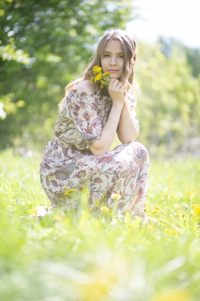 在一个温暖的阳光灿烂的日子里 一个疲惫而又迷人的女孩坐在公园的草坪上 手里拿着一束鲜花 — 图库照片