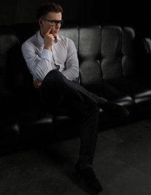 Beyaz gömlekli ve gözlüklü yakışıklı, kendine güvenen bir işadamı ofisteki koltukta oturuyor..