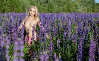 Güzel, çıplak bir sarışın güneşli bir yaz gününde çiçek açan bir tarlada yürüyor.