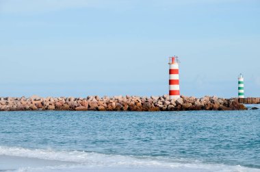 Portekiz 'in Faro şehrindeki plajda iki çizgili deniz feneri duruyor. Güneşli bir günde okyanusta küçük dalgalar.