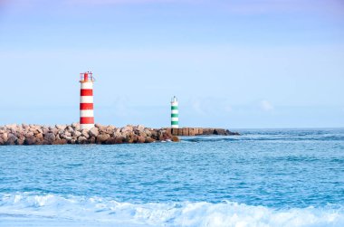 Portekiz 'in Faro şehrindeki plajda iki çizgili deniz feneri duruyor. Güneşli bir günde okyanusta küçük dalgalar.