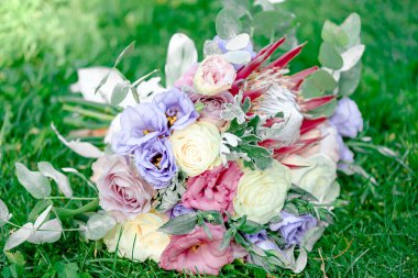 Bir buket beyaz gül ve yeşil yapraklı pembe ve menekşe Eustoma, güneşli bir günde yemyeşil çimenlerin arka planında bir fotoğraf