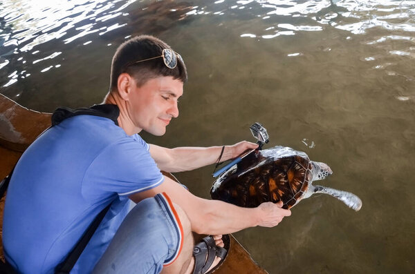 Young brunette guy with camera releases turtle into water, volunteer saves turtles, animal protection, boy takes pictures of turtle. saving animals  Sea Conservation Research Project  Center in Bento