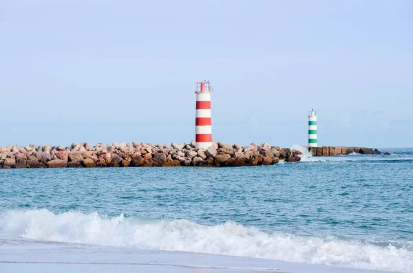 Portekiz 'in Faro şehrindeki plajda iki çizgili deniz feneri duruyor. Güneşli bir günde okyanusta küçük dalgalar.