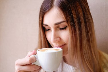 Yalnız sarışın kız pencerenin kenarında oturuyor elinde beyaz bir kupayla kalbi olan, romantik bir ruh hali içinde.