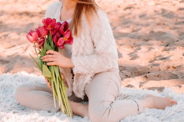 Güzel bir kız bir buket lale ile ekose üzerinde oturur. Şafakta güneşli romantik kahvaltı.