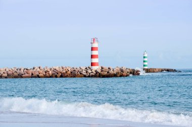 Portekiz 'in Faro şehrindeki plajda iki çizgili deniz feneri duruyor. Güneşli bir günde okyanusta küçük dalgalar.