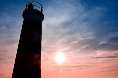Portekiz 'in Faro şehrindeki plajda çizgili bir deniz feneri standı. Karanlık bir akşamda okyanusta küçük dalgalar