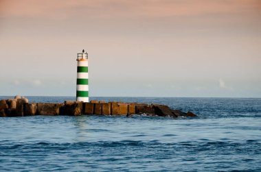 Portekiz 'in Faro şehrindeki plajda çizgili bir deniz feneri standı. Karanlık bir akşamda okyanusta küçük dalgalar