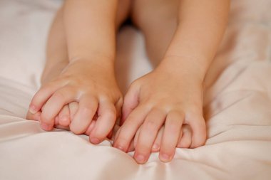 Çocukların elleri küçük bir çocuğun bacaklarına tutunur, bebek de parlak bir odada beşiğe oturur. Sıcaklık ve huzur, masaj.