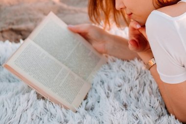 Güzel, sarışın bir kız ekoseye uzanıp kitap okuyor. Şafakta romantik kahvaltı, yaz sabahı. Çörekler ve çiçek laleleriyle fotoğraf çekimi