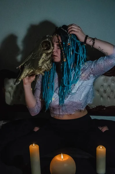 青いドレッドロックを持つ女の子は暗い部屋で夜に興奮し ろうそくの火と牛の頭蓋骨 — ストック写真