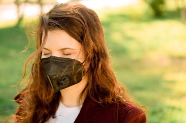 Sokakta çiçekli siyah maskeli bir kız. Kadın maskesini çıkardı, temiz hava aldı, karantina sırasında yürüdü.