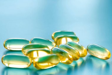 Mavi arka planda bir avuç dolusu omega 3 kapsülü 