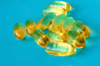 Mavi arka planda bir avuç dolusu omega 3 kapsülü 