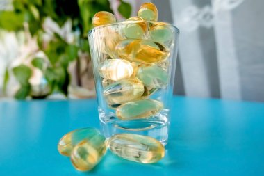 Omega 3 vitaminli cam bir bardak pencerenin yanındaki bir huş ağacının yanındaki mavi bir masada duruyor.