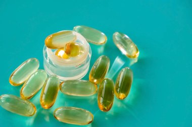 Bir avuç dolusu omega 3 kapsülü ve mavi bir sırt grubunda cam bir deney tüpü.