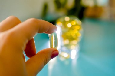 Kadın eli, şeffaf bir omega 3 kapsülü, huş ağacının dallarına yakın bir masada tabletlerle dolu bir bardak tutuyor.