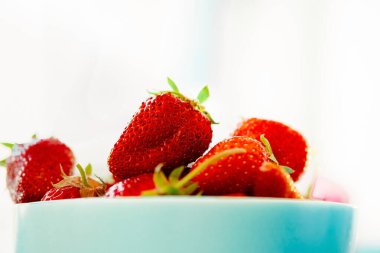 Kırmızı sulu olgun çilekler, açık arkaplanda mavi bir vazoda. Sağlıklı bahar kahvaltısı, meyve tabağı