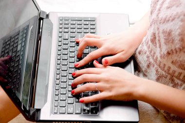 Hafif örgü kazaklı kız pencerenin yanında oturuyor ve elinde dizüstü bilgisayar tutuyor. Defterde kadın eli izi, evde uzaktan çalışma.