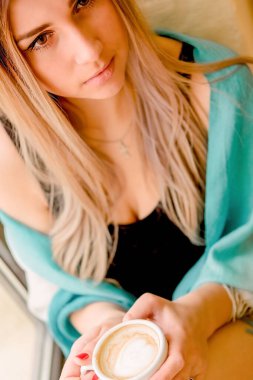 Şirin seksi sarışın elinde bir fincan kahve tutuyor. Güzel bir kadın pencere kenarında oturur ve nefis bir içkiden hoşlanır, sabah ayininden.