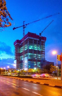 İdari bir kamu binasının gece fotoğrafı. İçinde kule vinçleri var.