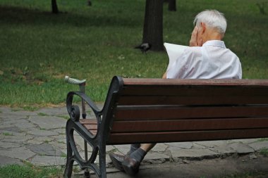 Yaşlı adam parkta bankta okuma