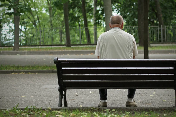 O homem está sentado no parque num banco. — Fotografia de Stock