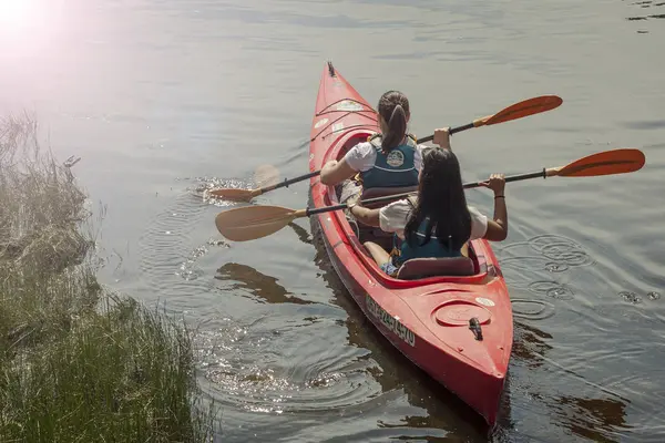 Two girls are swimming on the river in a red canoe