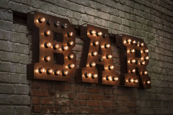 Яскраві літери BAR. Об'ємні літери з іржавого металу на цегляній стіні з гірляндою ламп розжарювання — стокове фото