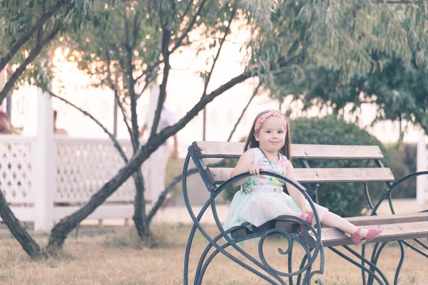 Очаровательная маленькая девочка сидит на скамейке — стоковое фото