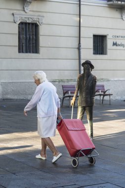 Pontevedra, İspanya - 19 Ağustos 2017: Yaşlı bir kadın kırmızı renkli büyük bir alışveriş arabasıyla yürüyor.
