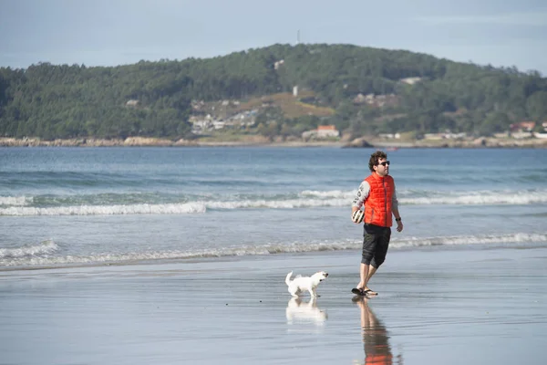 A man accompanied by a dog walks through the wet sand — Stockfoto