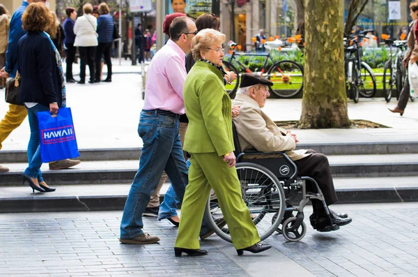 SAN SEBASTIAN, SPAIN - APRIL 5, 2014: A couple with an old man in a wheelchair walking in a central street of the city of San Sebatian (San Sebastian).