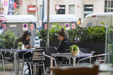 BARCELONA, SPAIN - 6 Kasım 2015: Kafeteryanın terasında oturan iki genç kadın, akıllı telefonlarını kontrol edin.