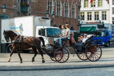 BRUGES, BELGIUM - 3 HAZİRAN 2015: Turistlerle dolu bir at arabası eski kasabanın sokaklarından birinde geziniyor.