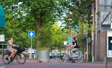 DELFT, NETHERLANDS - 6 Temmuz 2015: Her biri bisikletli iki kadın, köyün sokaklarından birinde yürüyor.