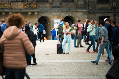 AMSTERDAM, NETHERLANDS - 8 HAZİRAN 2015: Cep telefonuyla konuşan, elinde bir buket çiçekle bir meydanın ortasında duran genç bir kadın.